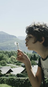 young girl blowing on dandelioon flower seeds with the mountains in the background