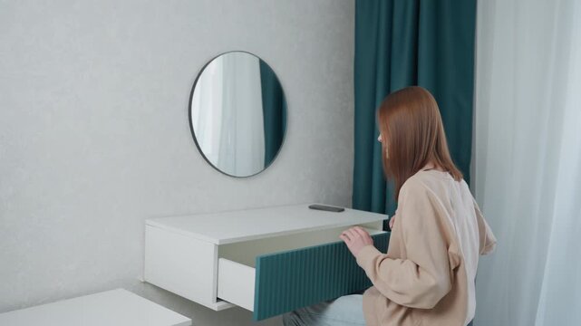 Young woman practices speech in mirror, self coaching session at vanity, opening drawer for notes, adjusting posture and expression, soft teal curtain, natural light, focused confidence building
