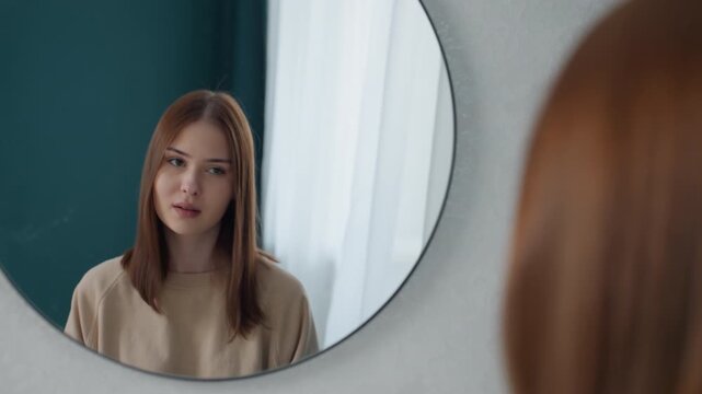 Young caucasian woman rehearsing confident presentation mirror steady eye contact teal curtain backdrop round wall mirror self coaching posture and speech rehearsal home studio vibe poised expression