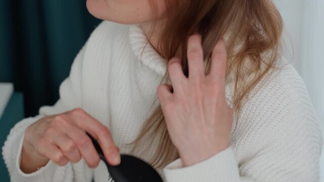 Caucasian woman coach detangling hair before virtual coaching session, closeup on hands and profile, checking split ends and frizz, anxious glance toward mirror, candid home routine preparing