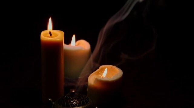Three magic Christmas wax candle flames calm burning in home in white smoke from incense aroma stick on black dark background with copy space. Closeup yoga, spa, wellness, relaxation. No people