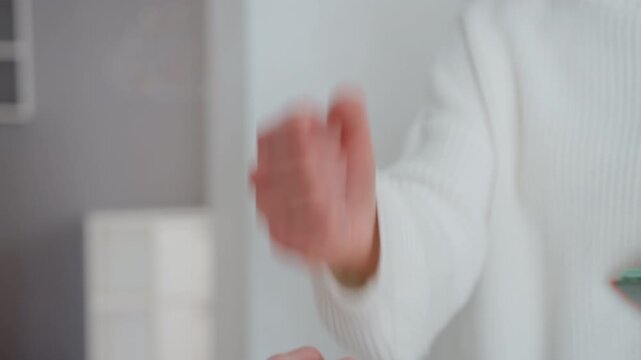 Closeup hands exchanging keys and notebook in quiet apartment hallway, female in white sweater reaches forward to accept item from visitor focus on textured sleeve, gentle grip, minimalist interior