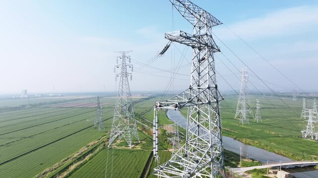 High voltage transmission towers standing tall above lush green fields and a winding river