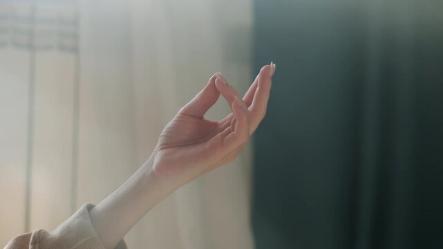 Sunlit hand gesture in cozy room, gentle mudra used by online tutor guiding breathing exercises, soft curtains, warm tones, closeup of fingers and palm, serene wellness atmosphere