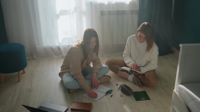 Sunlit study coaching scene caucasian mentor planning notes with student on floor, scattered notebooks and pens, collaborative discussion and strategy mapping, focused concentration, modern apartment