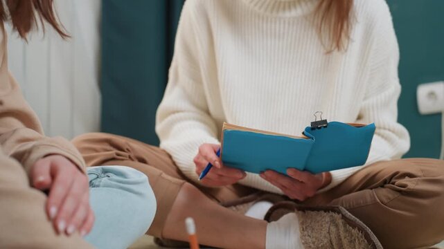 Home tutor session with blue notebook two people sitting crosslegged on floor in cozy room, tutor guiding student through grammar exercises, pen tapping pages, casual sweaters, warm natural light,