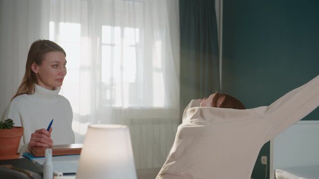 Caucasian tutor and student at home, cozy living room desk with lamp and notebook, gentle grammar coaching, patient corrections, student stretching then smiling, warm sunlight through curtain, relaxed