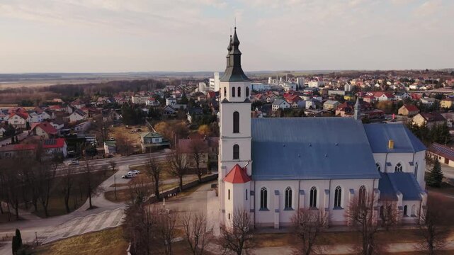 Drone Panorama Over Parish Church Piatnica With Blue Roof And Twin Towers, Village Rooftops Stretching To Horizon, Soft Evening Light, Calm Roads And Cemetery Backdrop, Cinematic Broll