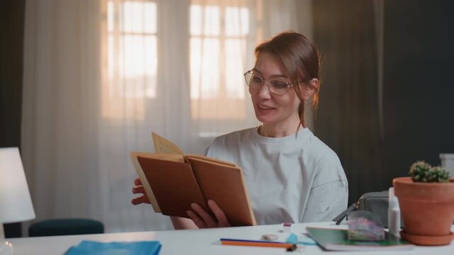 Cozy home scene white woman tutor reading grammar book at desk lit by warm lamp, wearing glasses and soft smile, explaining pronunciation and grammar rules during evening study session, notebooks