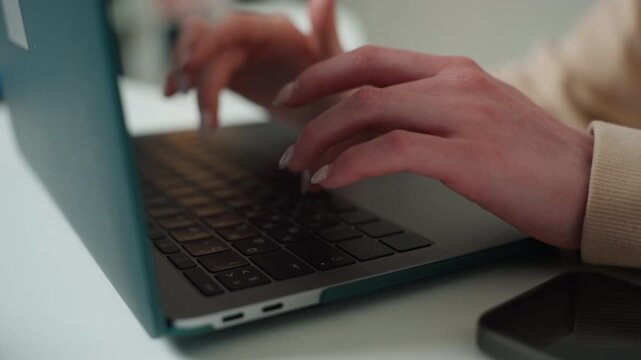 Hands of white coach typing on laptop in bright coworking corner, fast rhythmic keystrokes, smartphone nearby, live online feedback, deadlinedriven editing, focused productivity mood.