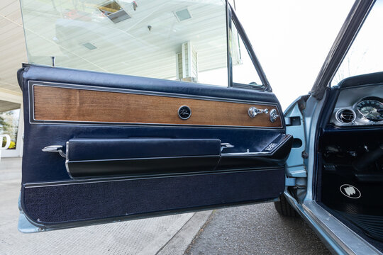 Vancouver, WA, USA - April 26, 2023 - Close up door panel of a blue 1963 Buick Riviera featuring Riviera emblem, wood grain trim, control panel, window switches, chrome accents and classic 1960s style