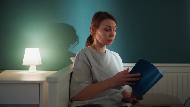 Sidelit caucasian tutor reading bedtime story from blue book, bedside lamp casting warm glow, calm expression and slow cadence, intimate home ritual promoting comfort and sleep in cozy bedroom
