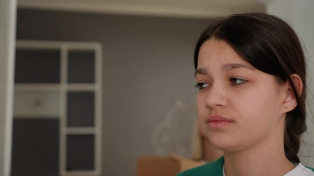 Young woman in new apartment stands near doorway with stacked boxes and tape, pensive expression capturing quiet uncertainty during moving day minimal modern interior, soft natural light, casual