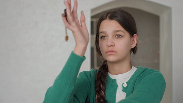 Girl pondering indoors. Young woman sitting thoughtfully. Emotionally reflective girl seated with keys in hand. Teen girl in empty apartment shows contemplative mood and nostalgia feelings