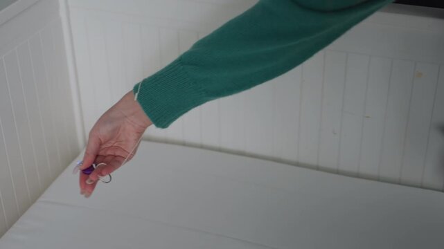 Woman checking mattress seam with light closeup hand shots using tiny key flashlight near corner while holding plant pot methodical renter movein inspection for stains and residue focused cautious
