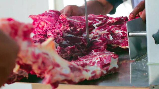 Raw meat slices being cut with a saw. Worker guides meat steadily for precise cuts.