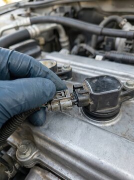 Technician's Gloved Hand Pulling Ignition Coil Off Valve Cover During Spark Plug Replacement