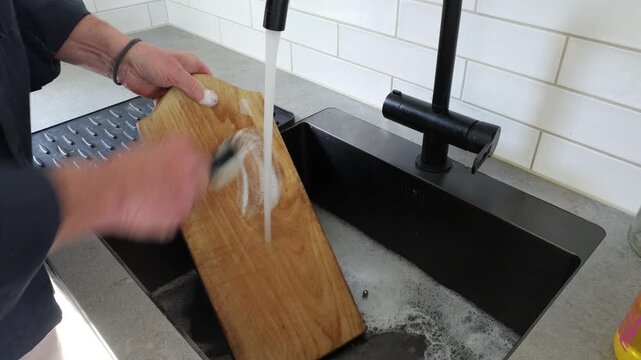 Stockholm, Sweden A man scrubs a wooden kitchen cutting board with soap and water. 