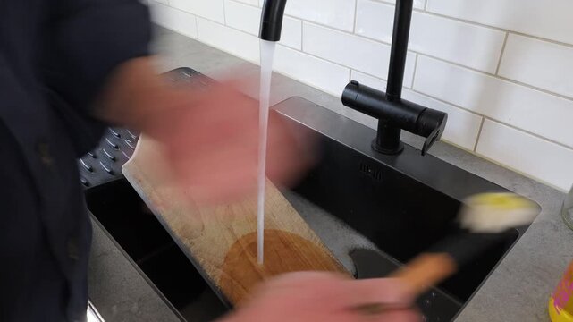 Stockholm, Sweden A man scrubs a wooden kitchen cutting board with soap and water. 