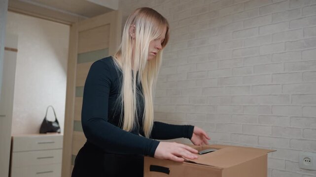 Blonde caucasian woman packing box doorway during move out, final walkthrough closing boxes, carrying carton to exit, checking latch, turning back for last glance, quiet nostalgic mood, empty