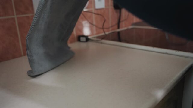Hands spreading towel on counter, tiled backsplash and sink visible, gray absorbent mat smoothed into place then yellow mug set down, routine morning setup during movein staging, tidy protective