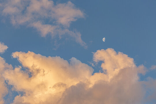 Half moon in sky framed by sunset clouds