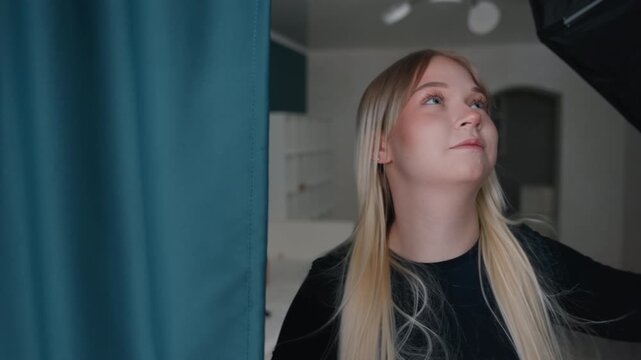 White blonde woman adjusting teal curtains with focused hands in new apartment, measuring placement, testing light and privacy, staging living space, methodical setup and calm DIY decor action