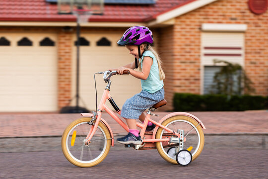 Panning movement shot of preschooler riding pink bike with training wheels on roadside