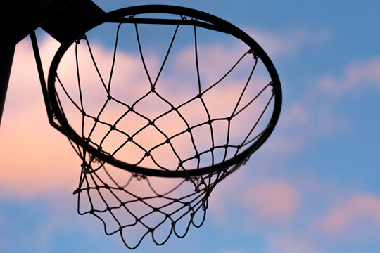 basketball net silhouetted against pastel dusk clouds in sky
