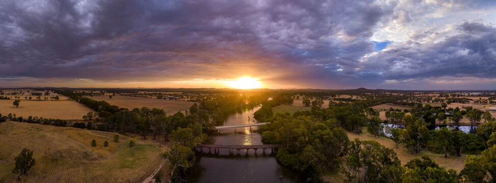 Aerial panorama view of colourful dramatic sunset over farmland alongside an inland river and bridge