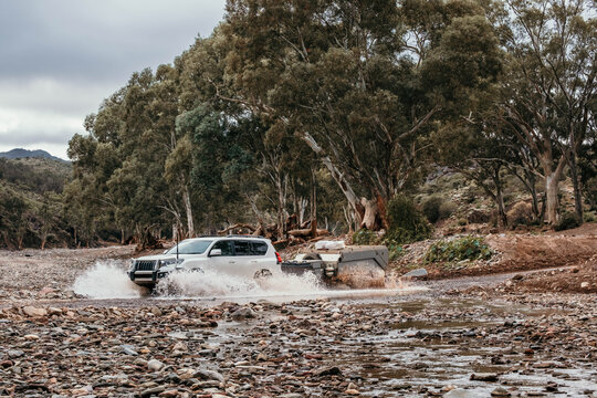 Four wheel drive tows camper trailer across river bed.