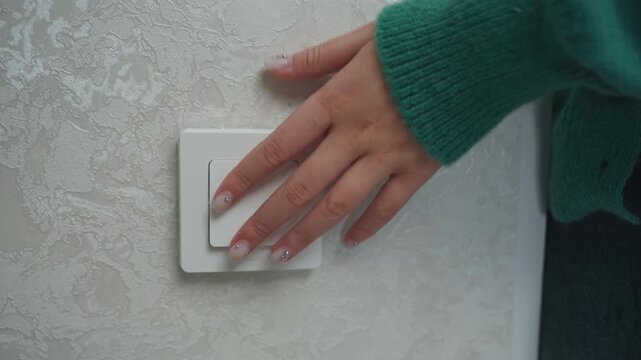 Hand testing light switch in new apartment interior, cozy textured wall and green sweater sleeve, closeup of fingers pressing switch during movein setup, renter checking electricity and lighting, calm