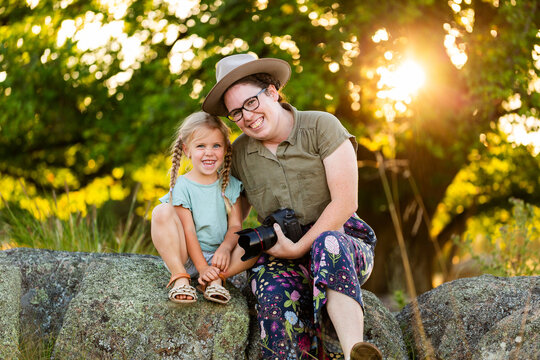 Photographer mum sitting with young kid on rock outdoors at photoshoot location
