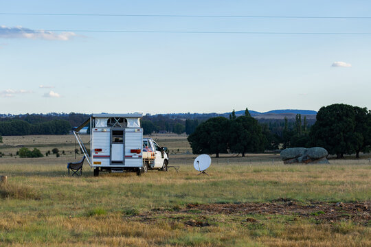 Camper trailer with satellite dish set up in paddock landscape