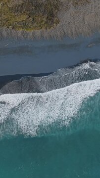 Aerial view of waves crashing on the black sand beach in Marokopa, New Zealand. The turquoise water meets the dark shore, creating a striking contrast.