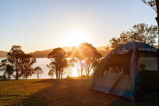 Tent pitched on hilltop in campground beside lake in golden Australian sunlight