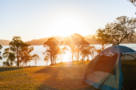 Tent pitched on hilltop in campground beside lake in golden Australian sunlight