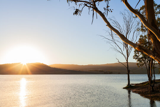 Sun setting across still scene of calm inland lake waters with sun dipping below horizon