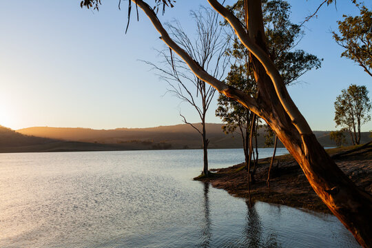 Sun setting across still scene of calm inland lake waters with sun dipping below horizon