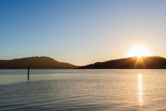 Sun setting across still scene of calm inland lake waters with sun dipping below horizon