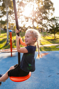 Happy little girl playing outdoors swinging on flying fox zipline at park playground