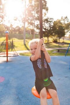Happy little girl playing outdoors swinging on flying fox zipline at park playground