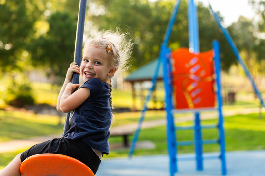 Happy little girl playing outdoors swinging on flying fox zipline at park playground
