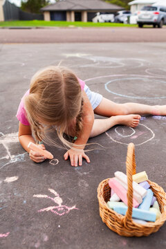 Basket of colourful chalk beside child drawing pictures on driveway  at home