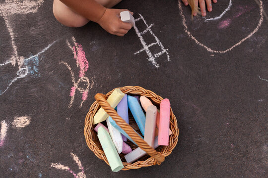 Basket of colourful chalk beside child drawing pictures on driveway  at home