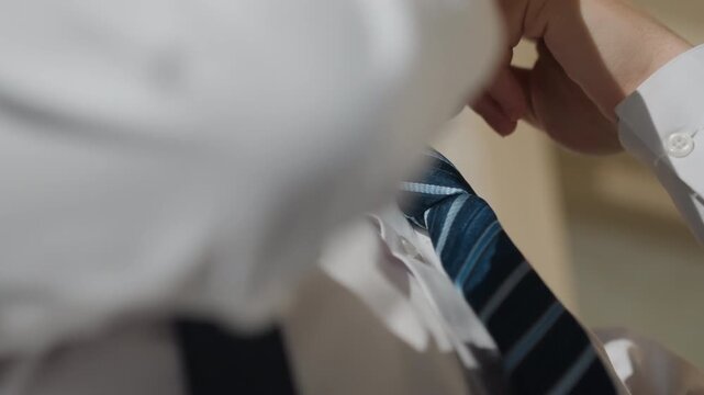 Young asian man tightening tie in hallway, white shirt and suspenders, steady hands making final adjustments, composed posture and groomed look, cinematic warm light, ready for presentation