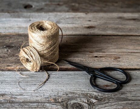 Natural jute twine rope spools and vintage metal scissors on aged rustic wood background, craft and DIY hobby supplies, farmhouse aesthetic