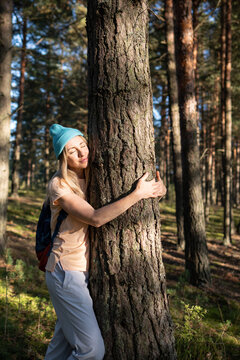 Calm woman hugging tree trunk in autumn forest with closed eyes at sunset. Relaxed female recreating in woods outside city on weekend spend day walking and wondering alone. Loving nature purity.