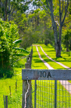 Driveway to house with vibrant green grass and wooden fence with house number in countryside