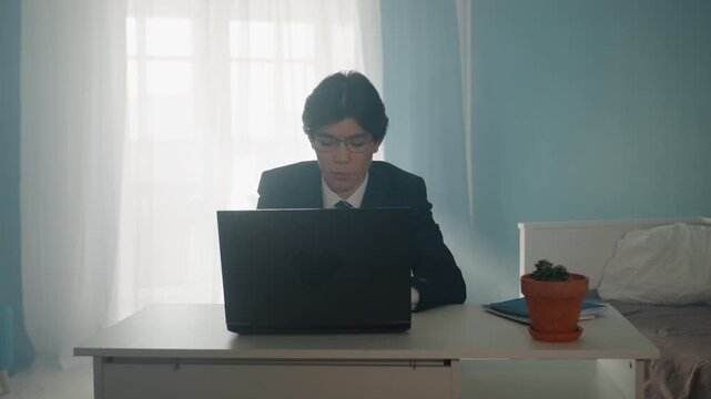 Focused worker reviewing emails. Young professional seated by window reviewing email and resume carefully. Male professional in office looks at laptop screen with intense focus and calm demeanor
